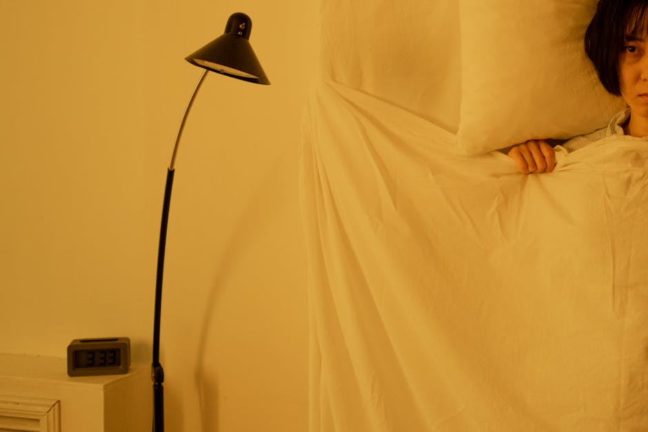 A person looking over white bedding next to a black lamp